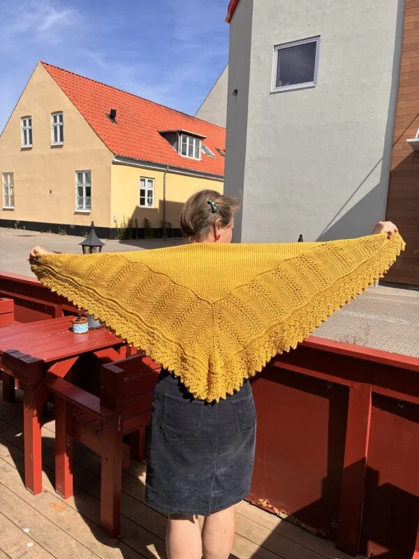 Karrygult håndstrikket svøb holdt ud over skuldrene med hulmønster og takket kant.