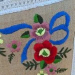 Nærbillede af blomsterbroderi på hør dug med blå sløjfe