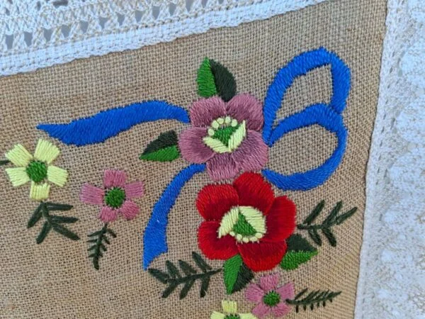 Nærbillede af blomsterbroderi på hør dug med blå sløjfe