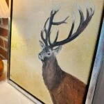 Oliemaleri af en hjort med stort gevir mod gylden baggrund i en smal, sølvfarvet ramme, set skråt.