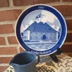 Blå-hvid årsplatte 1987 med Frederikshavn Toldkammer på holder; en blå kande, der ikke medfølger, står foran.