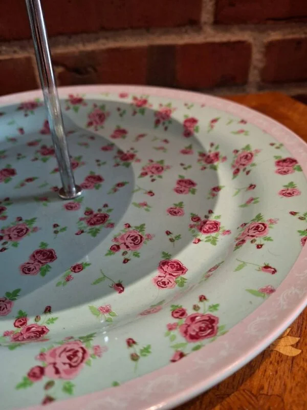 Detalje af kagefadets nederste etage med rosa roser, lys kant og sølvfarvet midterstang.