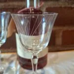 Nærfoto af et klart glas på fod med fine skrå linjer på kummen; et andet glas står bagved.