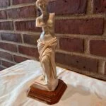 Venus de Milo statue i cremehvid med brun fod mod murstensbaggrund