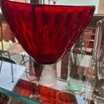 Rød glasskål på hylde ved siden af glas og flasker