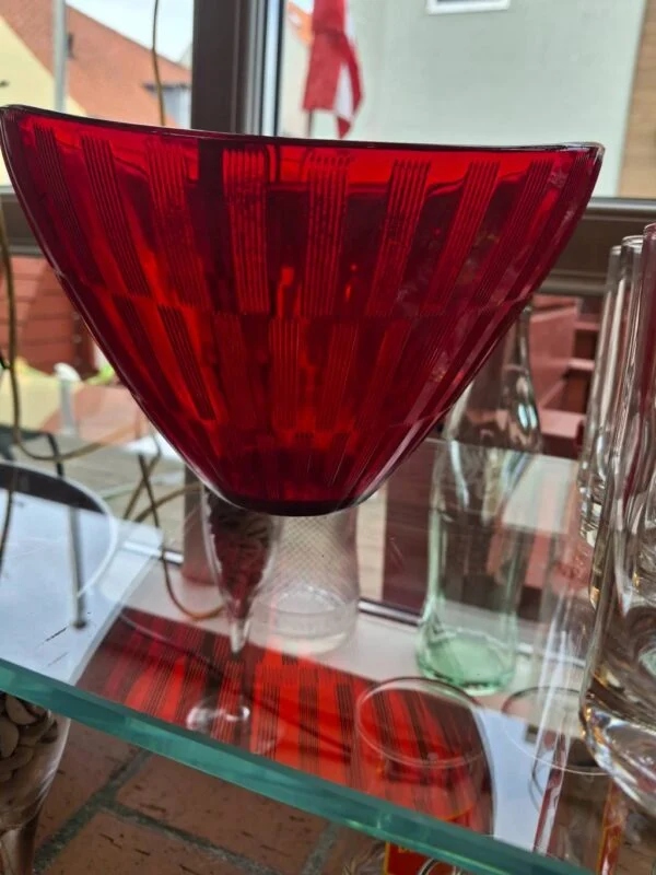 Rød glasskål på hylde ved siden af glas og flasker