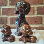 En stor brun hundefigur og to hvalpe på et klæde foran en murstensvæg.