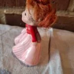 Pigefiguren set fra siden med løse røde hårfibre og folder i den lyserøde kjole.
