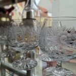 To klare glas med rund kumme, blomsterdekoration, kort stilk og mønstret fod.