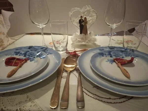 To kuverter med blå tallerkener, røde og guldfarvede navneflag samt en brudeparfigur mellem glassene. En inspirationsopstilling med flere separate varer.