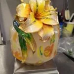 Vasens gule blomst og grønne blade set forfra, mens vasen står på en vægt.