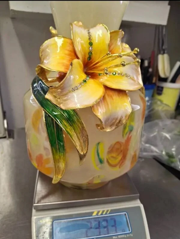 Vasens gule blomst og grønne blade set forfra, mens vasen står på en vægt.