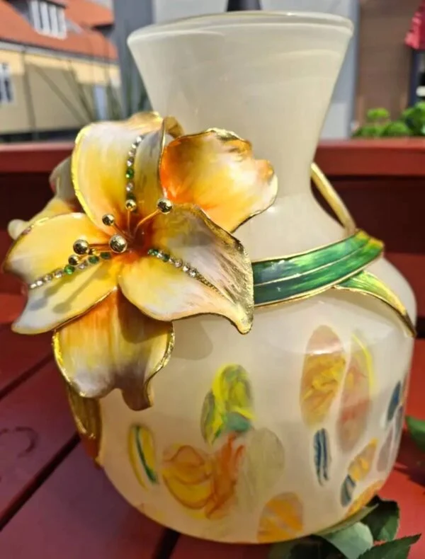 Nærbillede af vasens hals og påsatte gule blomst med grønne blade.