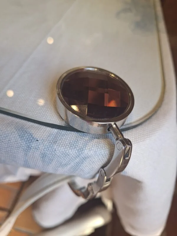 Lilla og gammelrosa taskeholder med udfoldet krog ved en bordkant