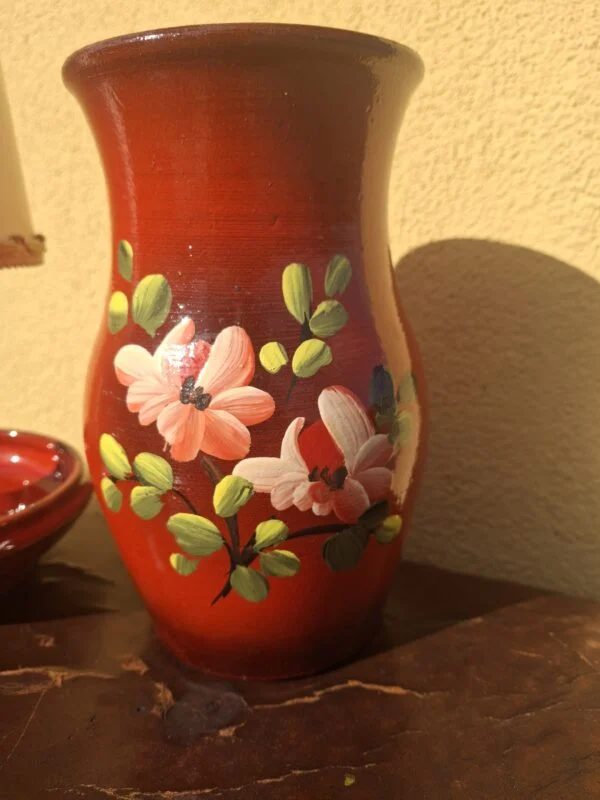 Rød vase med rosa blomster og grønne blade