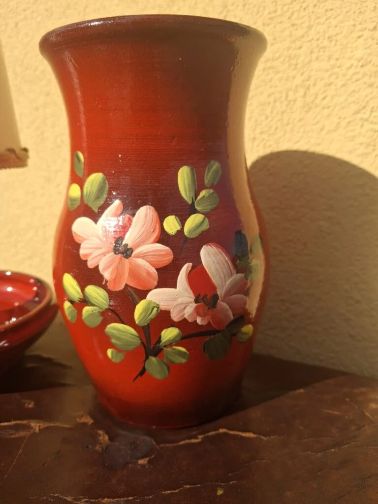 Rød vase med rosa blomster og grønne blade