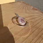 Ovalt vedhæng med rosa båndmønstret midterdel i en åben metalramme