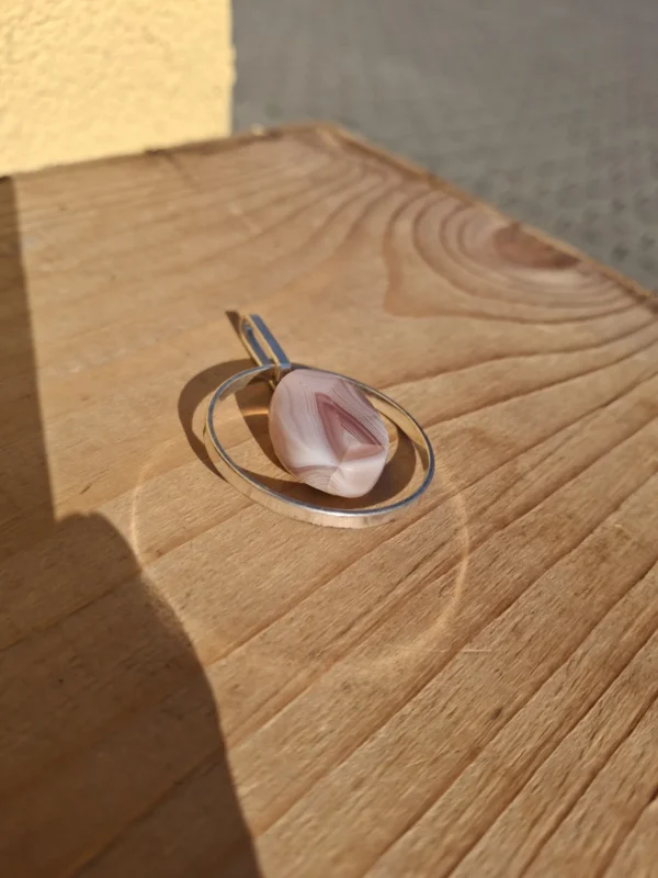 Ovalt vedhæng med rosa båndmønstret midterdel i en åben metalramme
