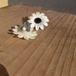 Hvid blomsterøreclips ved siden af en vendt øreclips med synlig clipslukning
