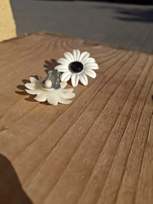 Hvid blomsterøreclips ved siden af en vendt øreclips med synlig clipslukning