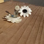 Åben metalclips med lys kontaktflade og synlige brugsspor bag en hvid blomsterøreclips