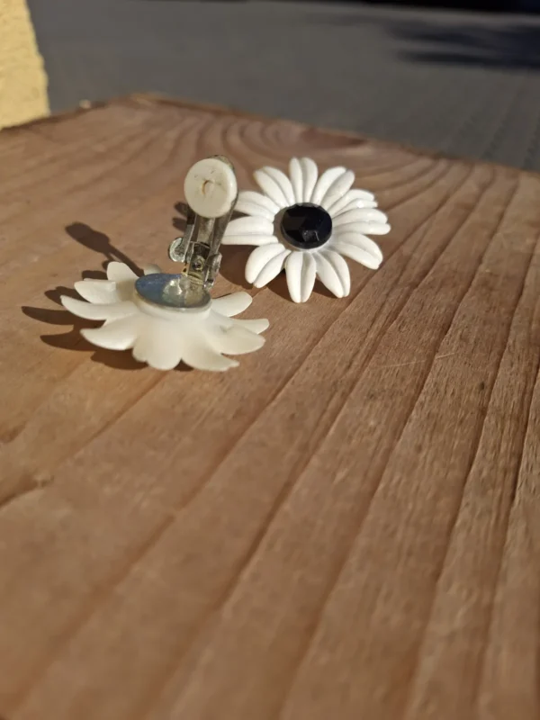 Åben metalclips med lys kontaktflade og synlige brugsspor bag en hvid blomsterøreclips