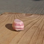 Afrundet rosa stenvedhæng med lyse bølgede bånd på den blanke forside