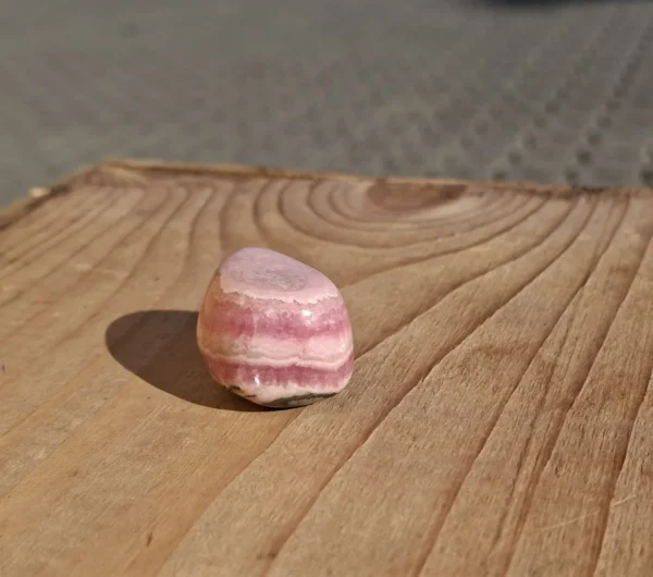 Afrundet rosa stenvedhæng med lyse bølgede bånd på den blanke forside
