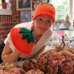 AI-genereret stemningsbillede baseret på VillaSnaks video: en kvinde med orange græskarhue og grøn top i en hyggelig vintagebutik.
