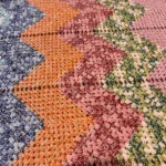 Originalt nærbillede af zigzagmønster og meleret garn i blå, orange, rosa og grønne farver.