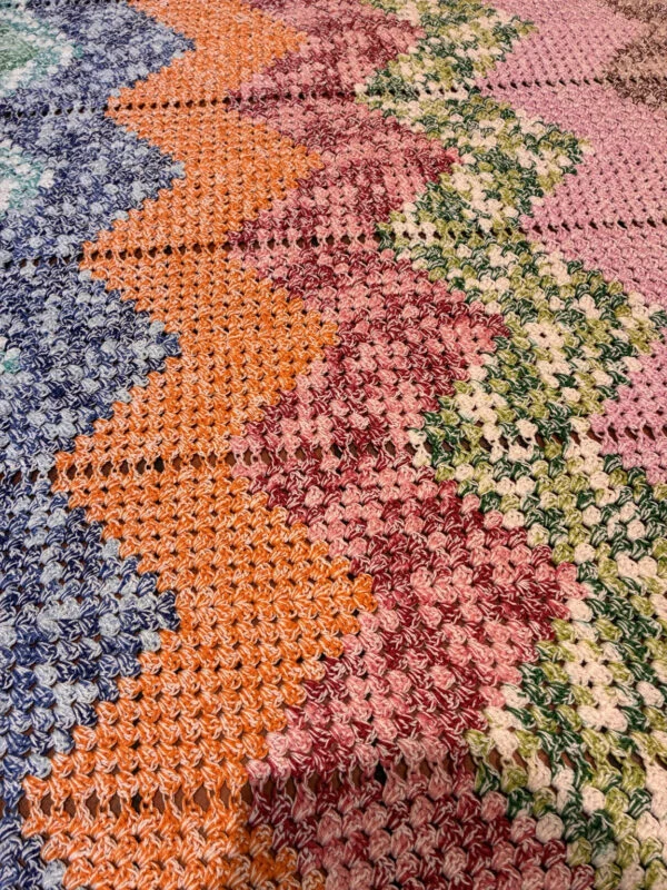Originalt nærbillede af zigzagmønster og meleret garn i blå, orange, rosa og grønne farver.
