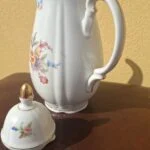 Blomstret porcelænskande med låget ved siden af og svungen hank