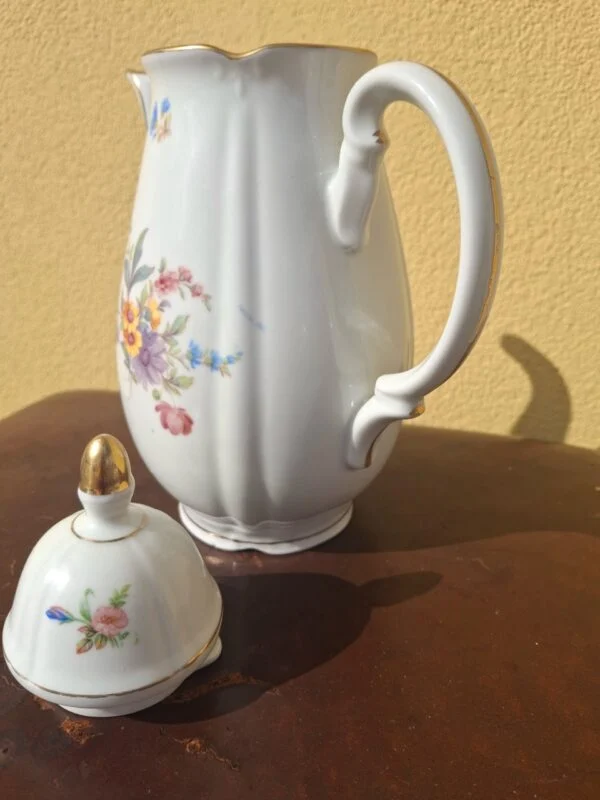 Blomstret porcelænskande med låget ved siden af og svungen hank