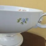 Blå blomster på den hvide skåls side og gulddetaljer på foden