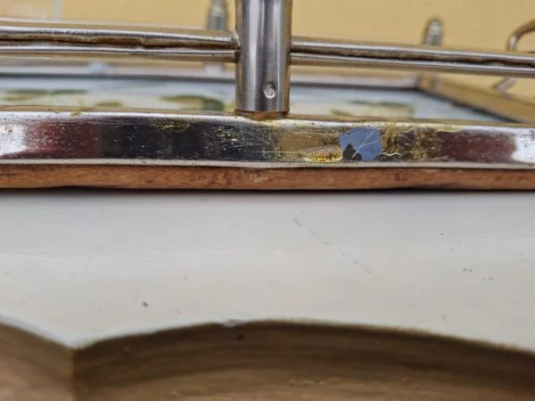 Nærbillede af glasbakkens metalramme med ridser og afskalning i overfladen