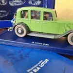 Grøn sedan med mørke skærme og Tintin bagpå, på soklen Le Lotus Bleu