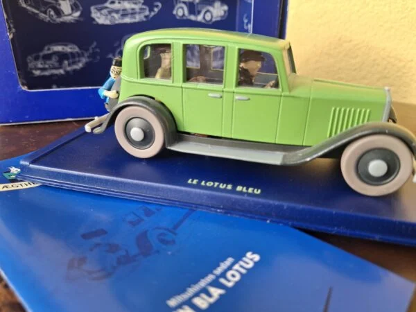 Grøn sedan med mørke skærme og Tintin bagpå, på soklen Le Lotus Bleu