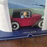 Rød Tintin-modelbil i klar udstillingskappe med illustreret baggrund