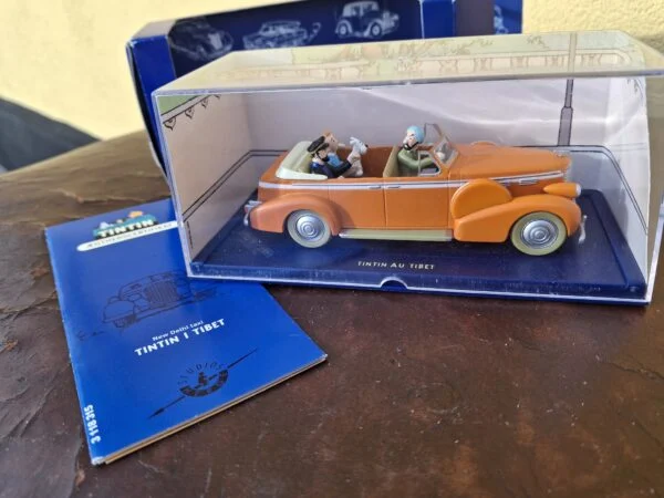 Tintin-modelbil under klar kappe sammen med blå æske og hæfte