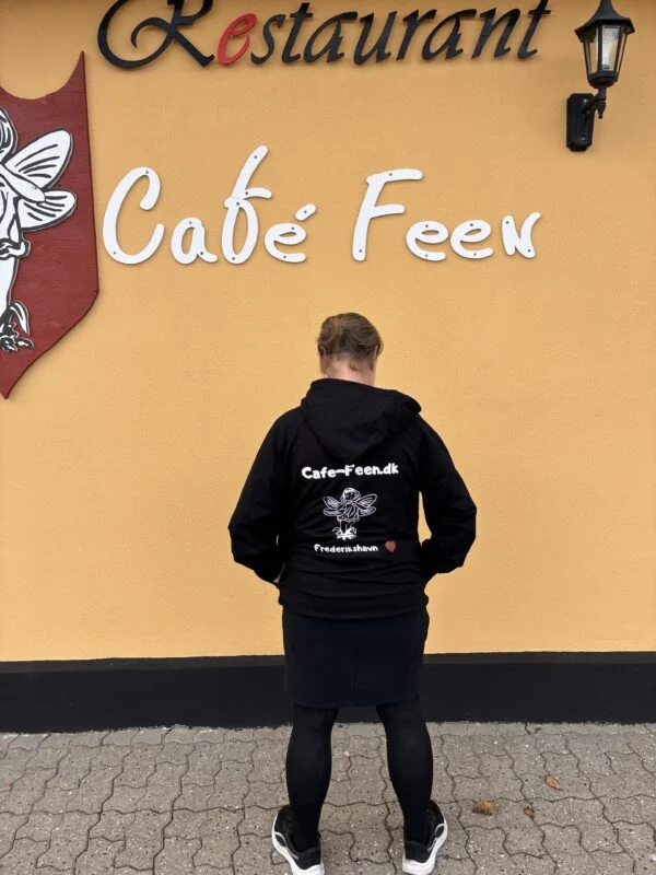 Café Feen hoodie vist bagfra under caféens skilt