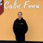 Charlotte i sort Café Feen hoodie foran caféens skilt i Frederikshavn