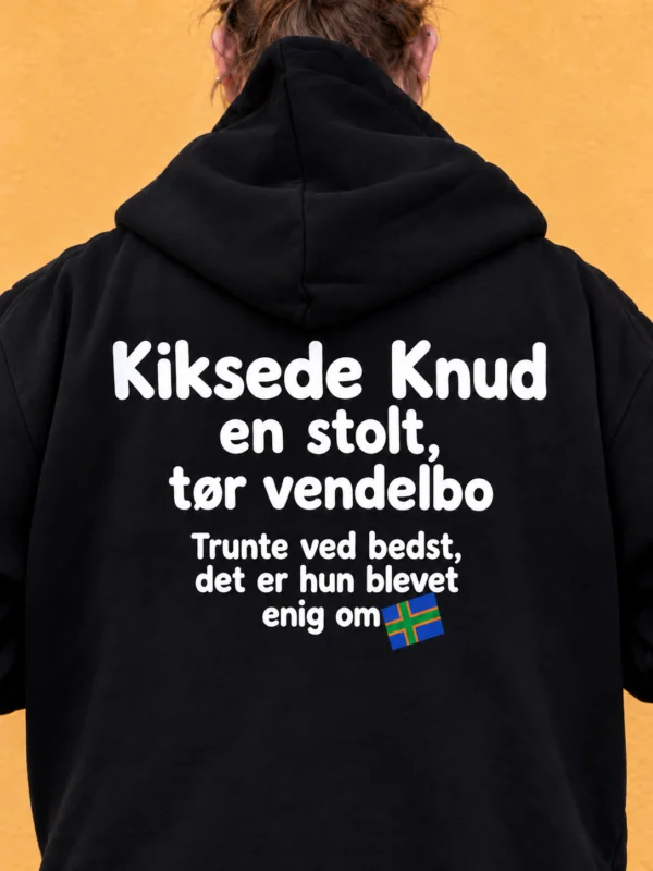 Kiksede Knud hoodie med “Trunte ved bedst, det er hun blevet enig om” og skråt blåt vendelboflag med grønt kors og orange kant på ryggen – AI-visualisering